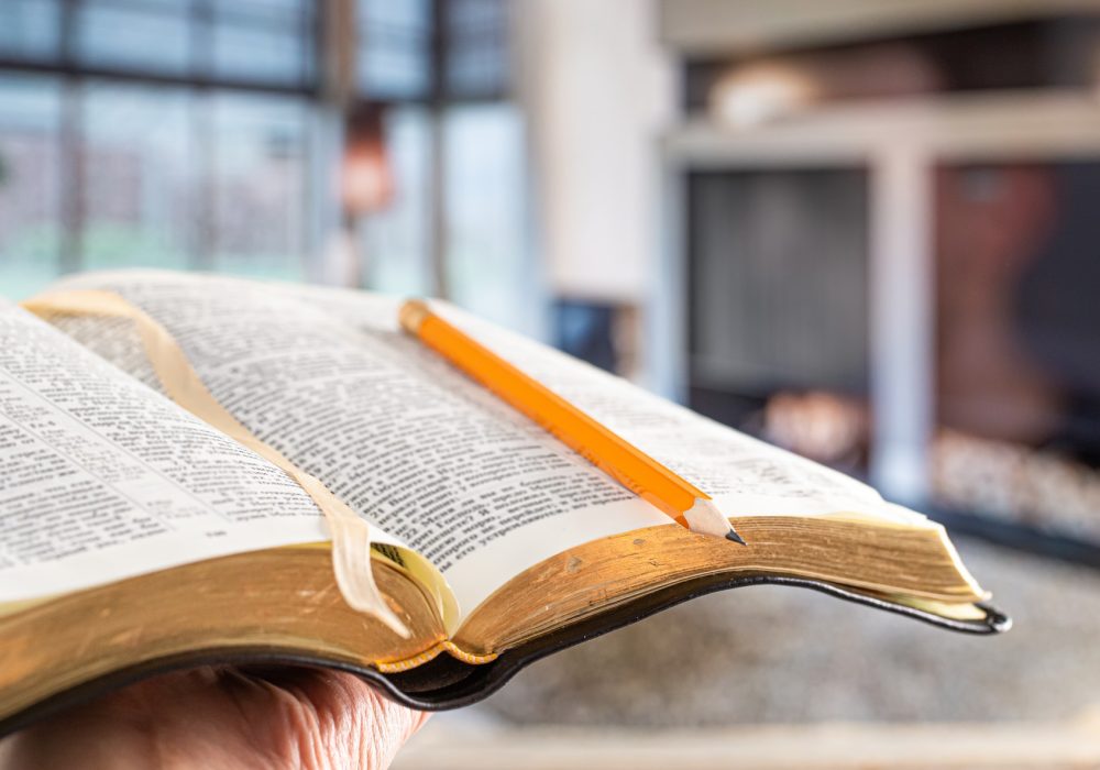 A man holds a Bible with a pencil, against the background of the living room.