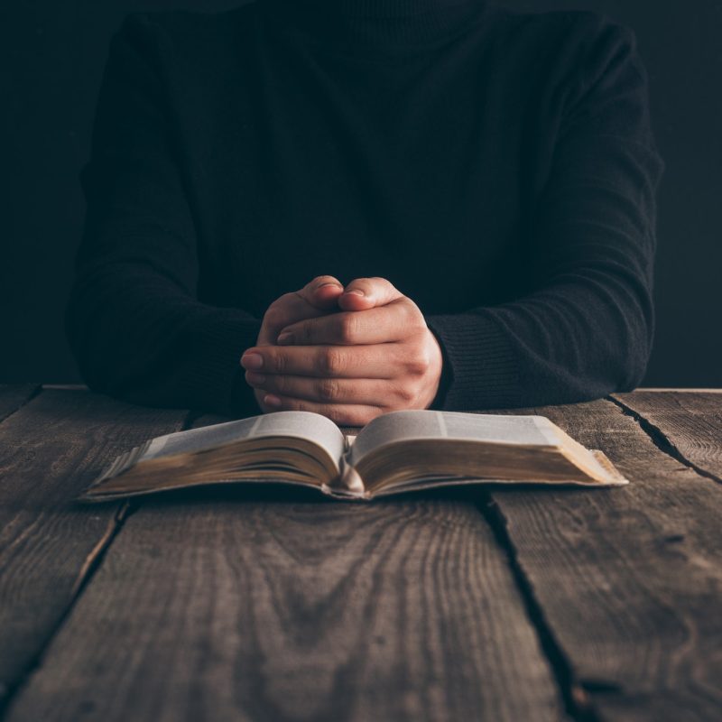 cropped image of nun sitting at table with bible and praying