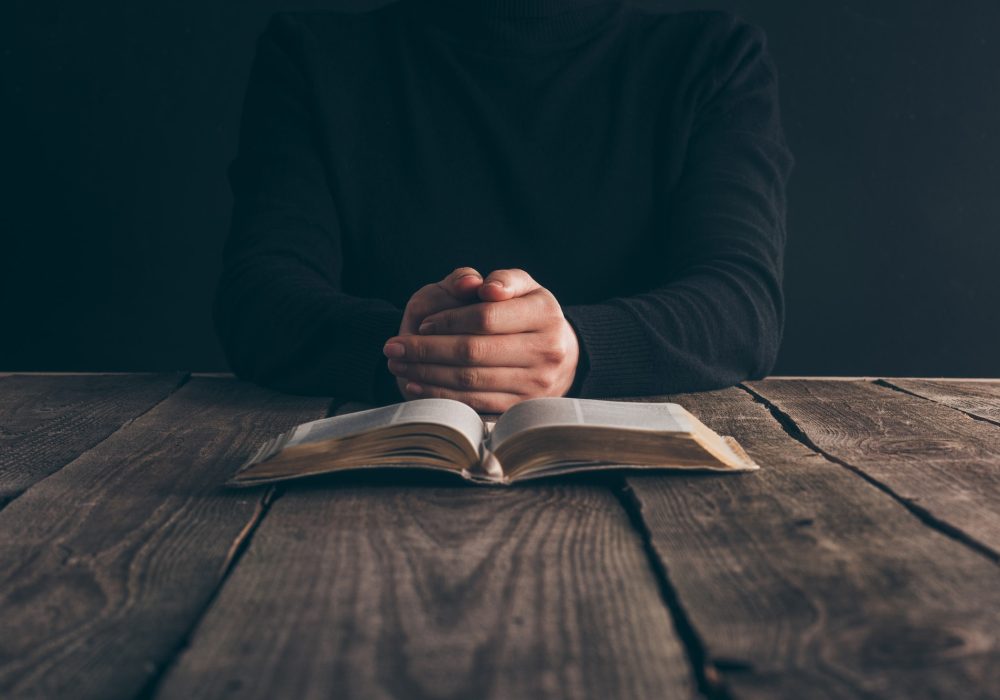 cropped image of nun sitting at table with bible and praying